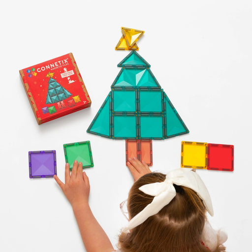 Child building a magnetic Christmas tree with Connetix tiles beside the pack