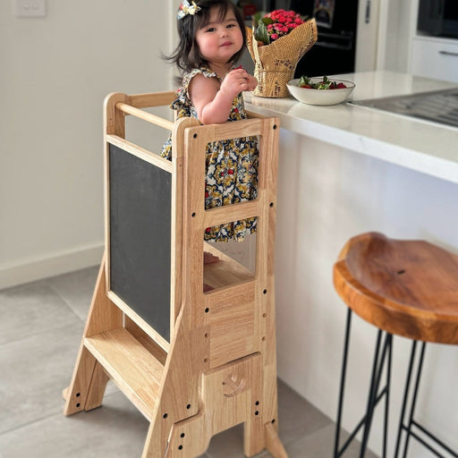 Toddler standing in the myduckling learning tower at a kitchen bench with the chalkboard side facing out